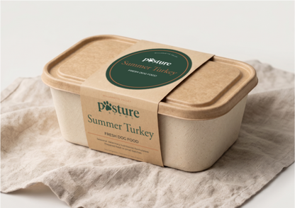 A square biodegradable container of Posture Summer Turkey fresh dog food, wrapped in a kraft paper band with a green circular label, resting on a textured beige linen cloth against a white background.